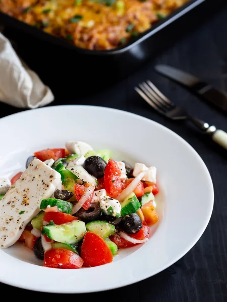 Siyah bir tablo üzerinde beyaz bir tabak içinde Yunan salatası.