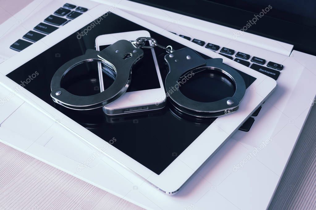 Handcuffs on electronic devices (laptop, pad, phone). Punishment for crimes in the network. Toned photo.