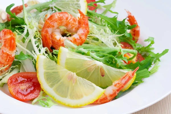 Salad with rocket salad, tomato and shrimp on a white plate. Close-up