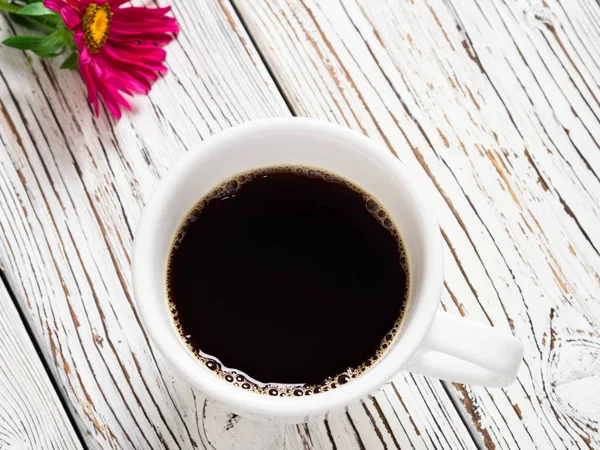 Eski ahşap bir masada bir fincan kahve ve kırmızı bir çiçek.