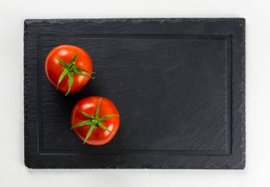 Yeşil yapraklı taze domatesler siyah servis tabağında izole edilmiş.