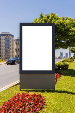 Şehir caddesinde dikey olarak parlayan bir reklam panosu var. Arka planda binalar ve arabalar var..