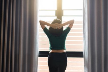 Evde yatak odasında başının üzerinde elleri ile kadın rahatlatıcı ve pencere yakınında duran Arka görünümü