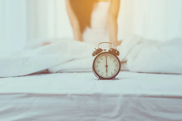Close up of alarm clock at 6 o\'clock in the morning and blurred woman waking up in her bedroom