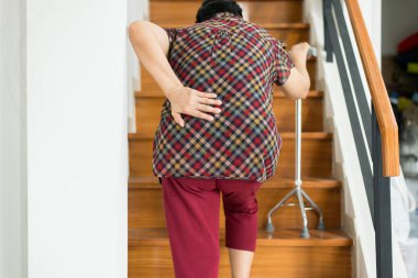 Asian elderly older woman suffering from low-back lumbar pain while walking on stair at home