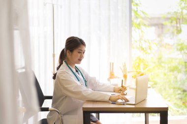 Doktor Asyalı kadınlar oturma ve hastanede dizüstü bilgisayar ve not yazma kullanarak masa üzerinde çalışan, Dizüstü bilgisayar klavyesi üzerinde kadın yazma 