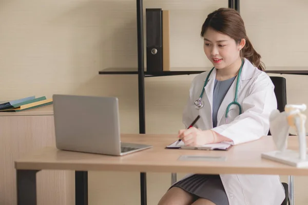 医師の美しいアジアの女性は ノートパソコンを使用して机の上に座って作業し 病院でメモを書く — ストック写真