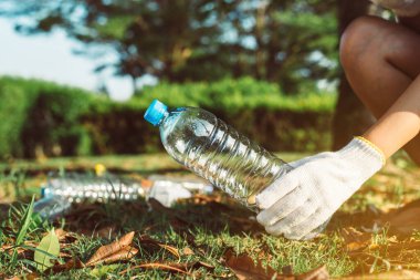 Gönüllü kadın elleri eldiven takıyor ve halka açık parktaki çimlerden plastik şişeyi uzak tutuyor, geri dönüşüm ve atık yönetimi kavramını ortadan kaldırıyor, çevre dostu