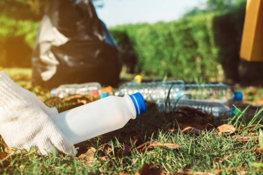 Gönüllü kadın elleri eldiven takıyor ve halka açık parktaki çimlerden plastik şişeyi uzak tutuyor, geri dönüşüm ve atık yönetimi kavramını ortadan kaldırıyor, çevre dostu