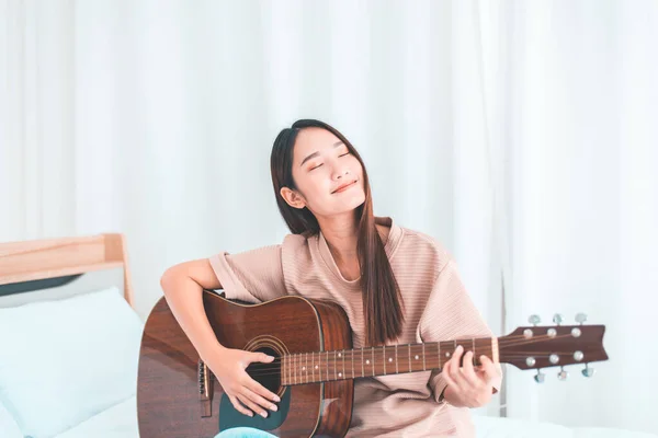 幸せな若いですアジアの女性遊びギターでベッドルームに自宅 — ストック写真