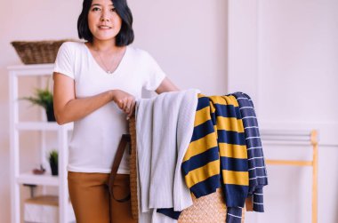 Mutlu Asyalı kadın evde sepetle çamaşır yıkıyor.