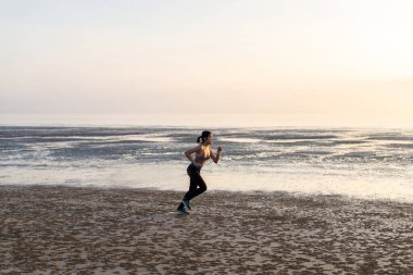 Gün batımında sahilde koşan sağlıklı Asyalı kadın.