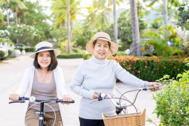 Mutlu son sınıf Asyalı kadın kızıyla bisiklet sürüyor. Halk parkında, sağlık sigortasında ve yaşlı bakım konseptinde.