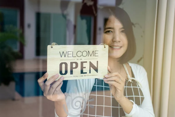 Happy asian woman owner turning open sign after lockdown quarantine in modern coffee shop