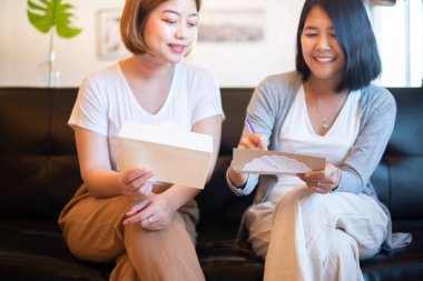 Mutlu Asyalı iki kadın bir sonraki tatil için evdeki kanepede oturmuş tebrik kartı yazıyor.