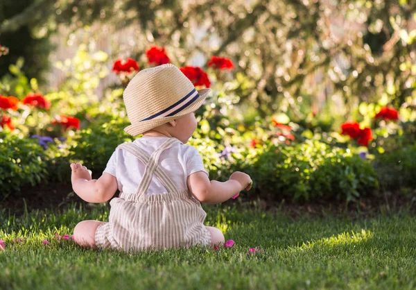 美しい春の日に庭で花を見て草の上に座っている赤ちゃん — ストック写真