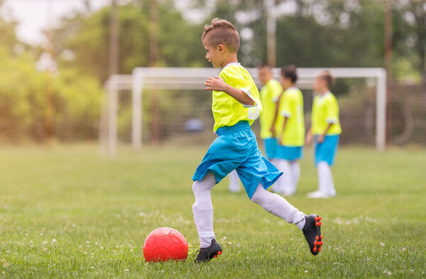 Мальчик пинает футбол на спортивном поле во время футбольного матча
