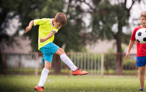 Мальчик пинает футбол на спортивном поле во время футбольного матча
