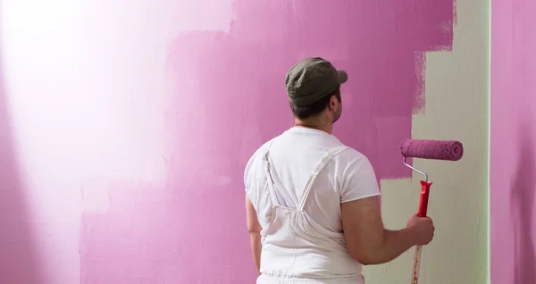 Young man is painting wall with painting roller