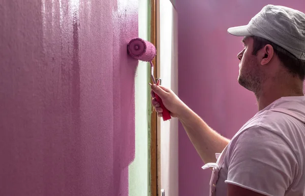 Young man is painting wall with painting roller