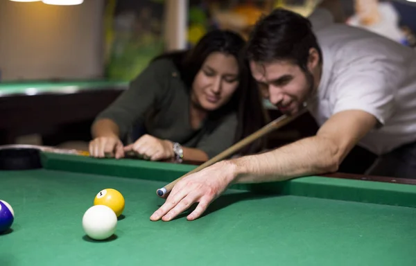 Handsome guy and a beautiful girl are playing billiards he is teaching her how to play