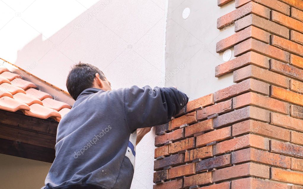 Worker putting red bricks on the house wall 