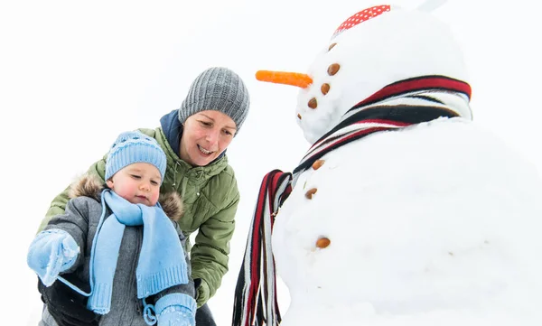 Glimlachend jongetje en zijn moeder gebouw sneeuwpop — Stockfoto