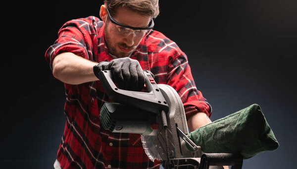  Красивый человек с помощью современной электрической циркулярной пилы в мастерской
