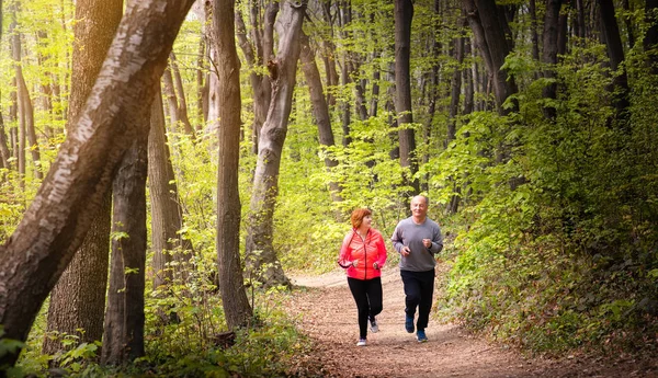 Husbanf and wife wearing sportswear and running in forest