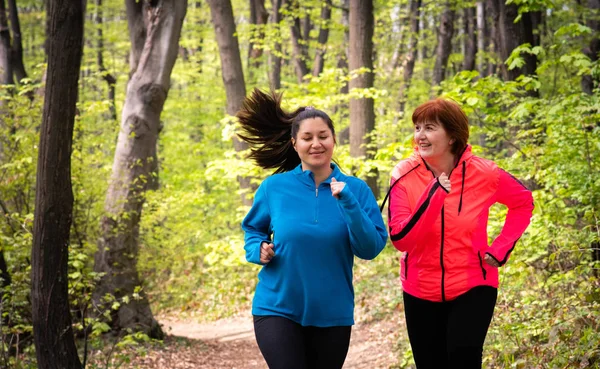 Madre e figlia indossano abbigliamento sportivo e corrono nella foresta — Foto Stock