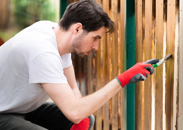 Schöner junger Mann bemalt Holzoberfläche mit Pinsel — Stockfoto