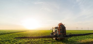 Traktör gün batımında soya tarlası püskürtüyor.