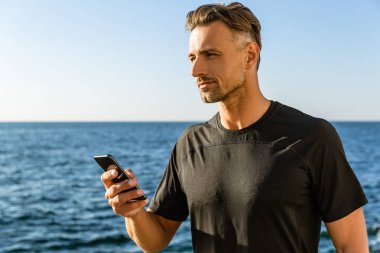 deniz kıyısı ve uzağa bakarak smartphone yakışıklı yetişkin adam