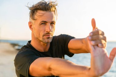 close-up shot of handsome adult sportsman stretching hand before training on seashore clipart