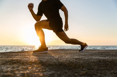 cropped shot of athletic man doing lunges during training on seashore