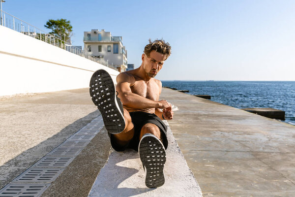 handsome adult shirtless sportsman doing side crunches on seashore