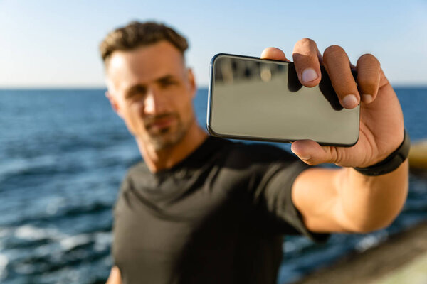 close-up portrait of adult man taking selfie with smartphone on seashore