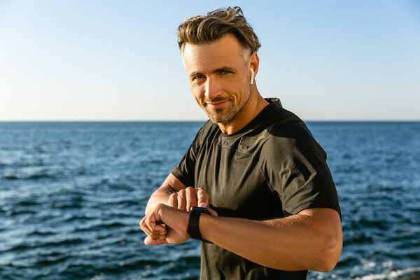 happy adult man with wireless earphones and smart watch on seashore