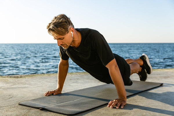 adult sportsman with wireless earphones doing push ups on seashore