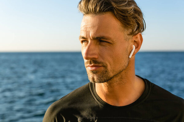 close-up portrait of handsome adult man with wireless earphones on seashore looking away