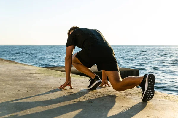 athletic sprint runner in start position for run on seashore