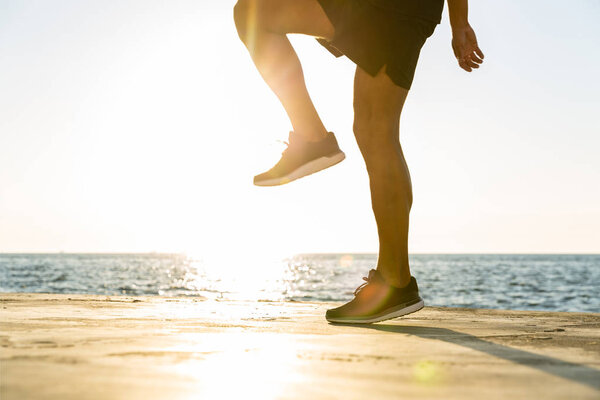 cropped shot of sportsman working out on seashore in front of sunrise