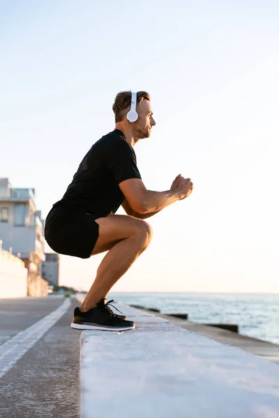 Side View Athletic Adult Man Headphones Standing Squats Parapet Seashore — Free Stock Photo