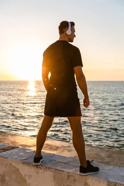 Rear View Athletic Adult Man Headphones Standing Seashore Front Sunrise — Stock Photo, Image