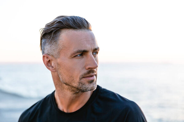 close-up portrait of handsome adult man with grey hair looking away on seashore