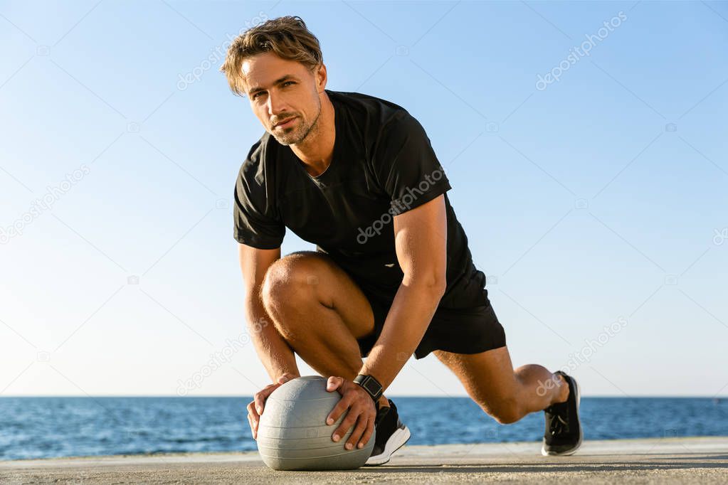 handsome adult sportsman working out with fit ball on seashore