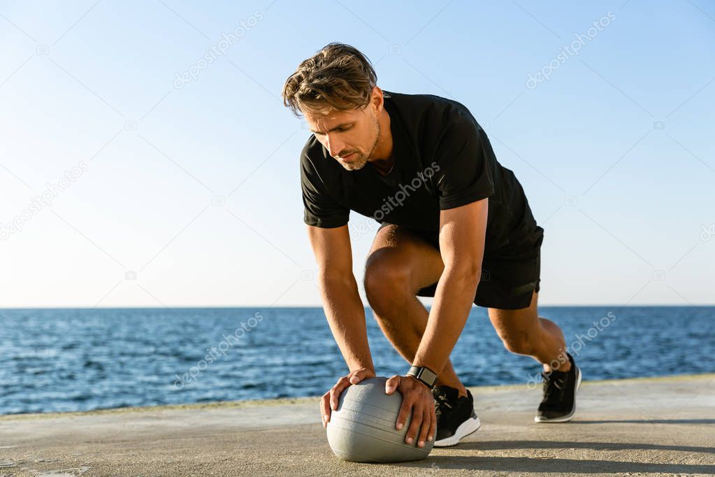 handsome adult sportsman doing push ups with fit ball on seashore
