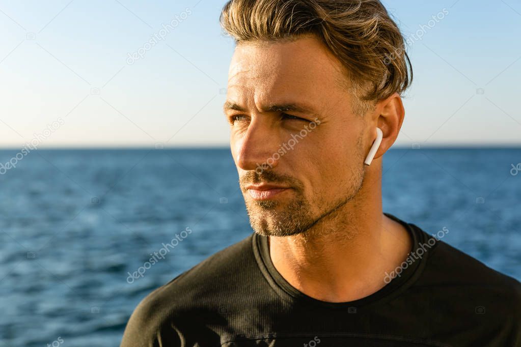 close-up portrait of handsome adult man with wireless earphones on seashore looking away