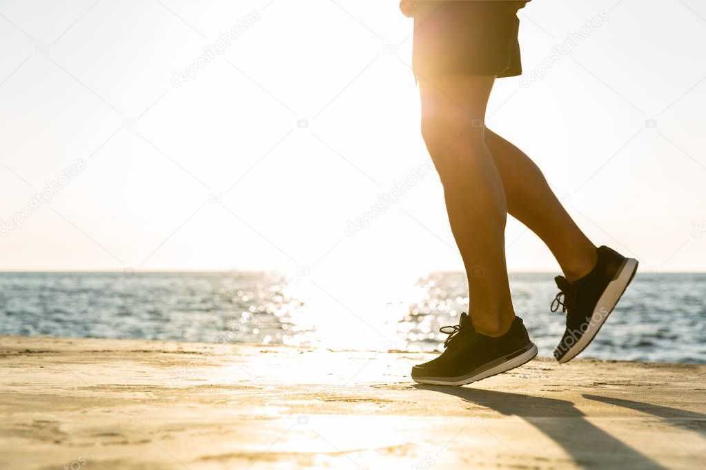 cropped shot of sportsman jogging on seashore in front of sunrise