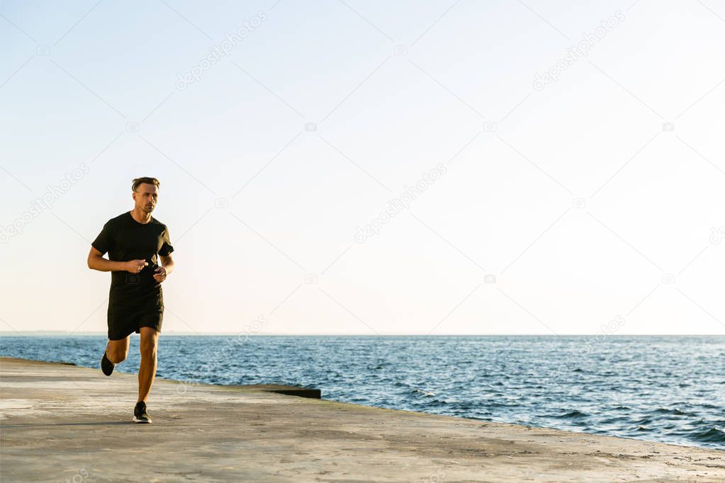 handsome adult sportsman jogging on seashore in morning